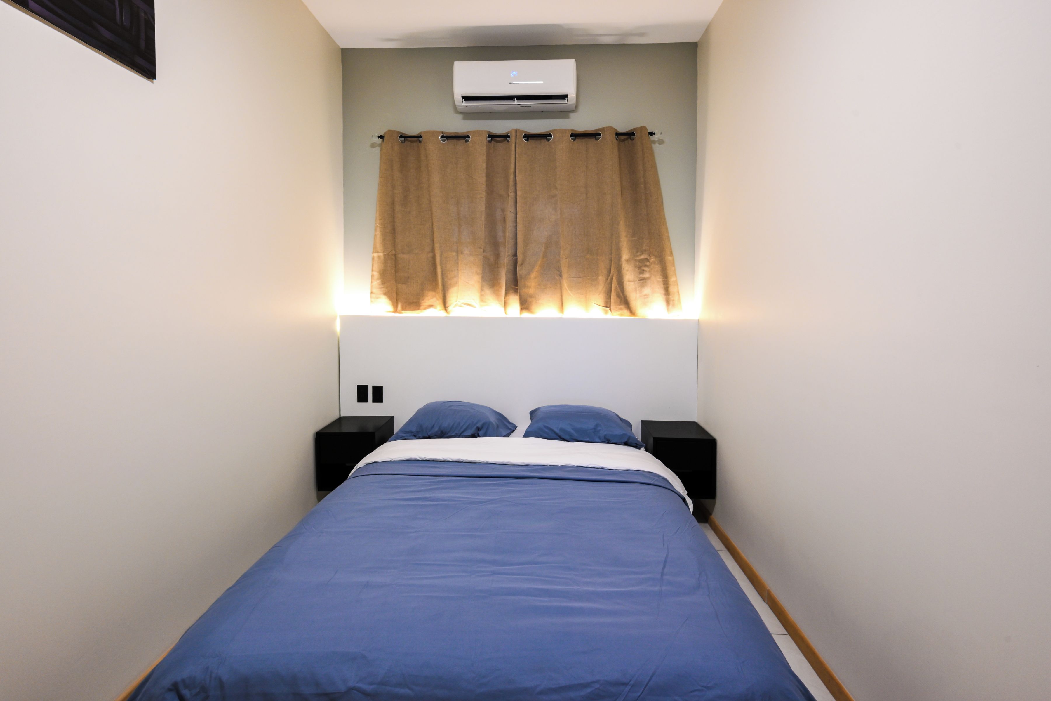 Une chambre à coucher comprenant un lit, des tables de chevet, un appareil de climatisation et un rideau.