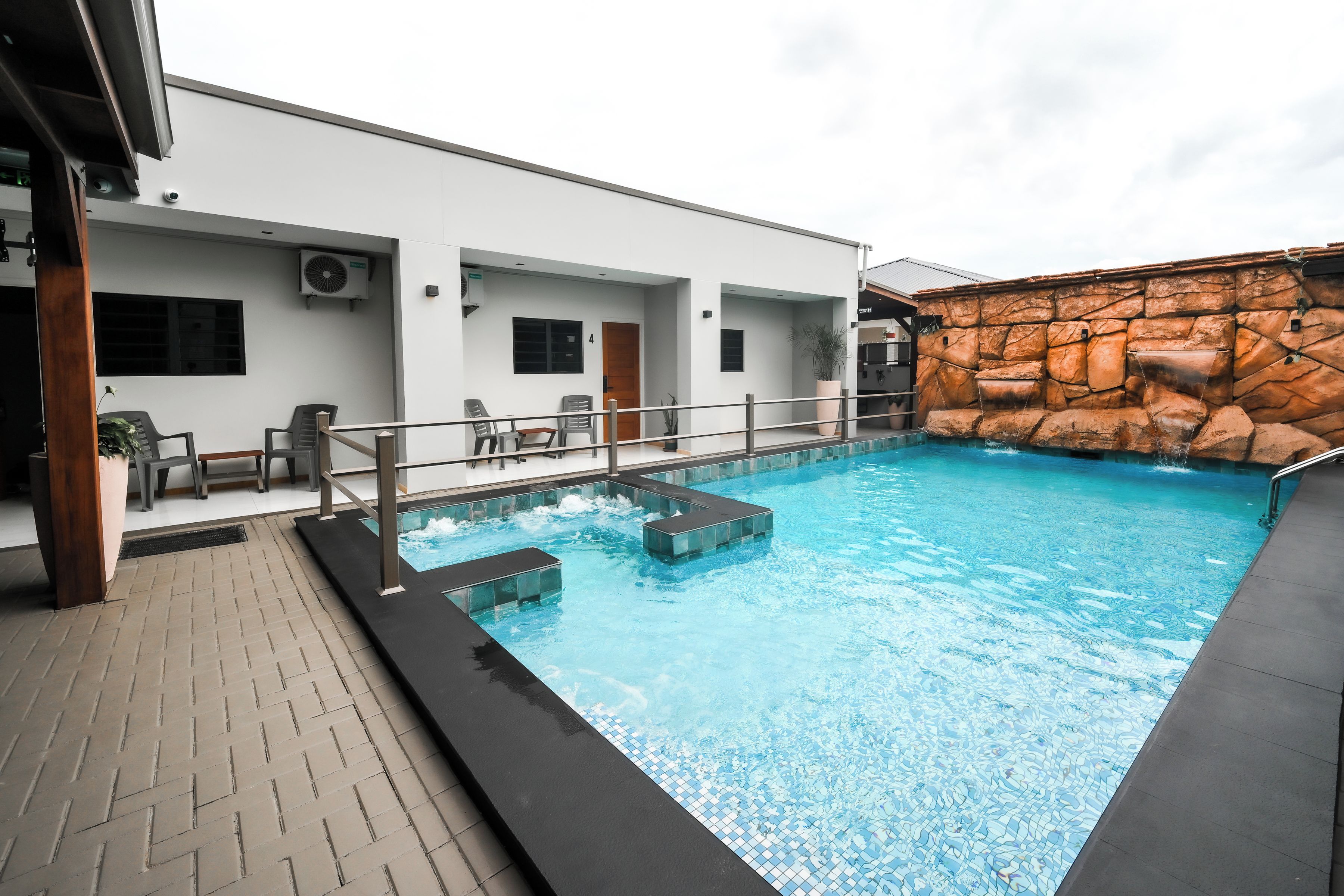 A swimming pool with a stone wall and a covered seating area with chairs.