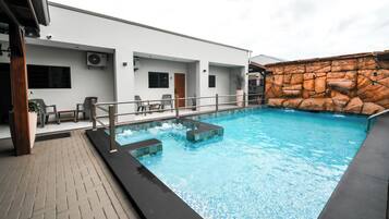 A swimming pool with a stone wall and a covered seating area with chairs.