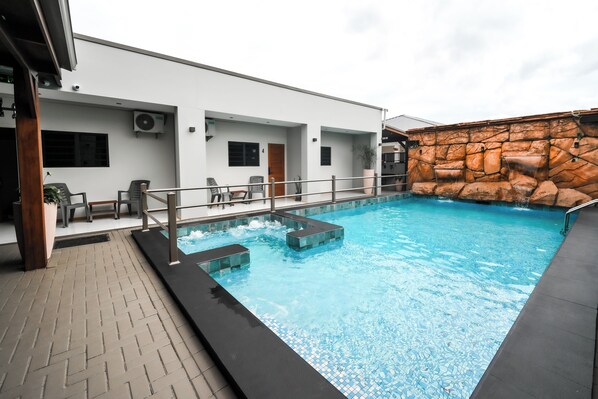 A swimming pool with a stone wall and a covered seating area with chairs. - Lure Boutique Hotel (Paramaribo)