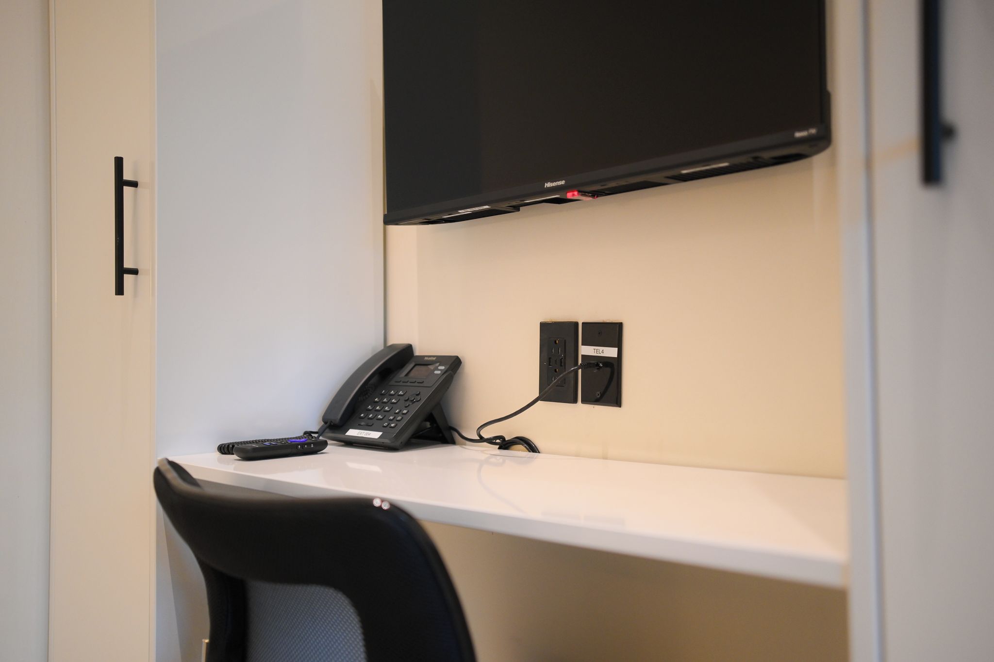 A hotel room with a desk, a telephone, and a television mounted on the wall.