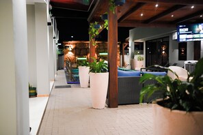 Un patio interior con asientos, plantas en macetas y una pantalla de televisión mostrando un programa.