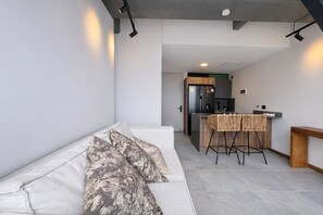 Un espai de vida modern amb un sofà, una cuina i un tamboret.