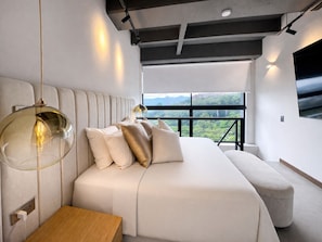 A modern bedroom with a large bed, a bedside table, and a view of a cityscape through a large window. - Luxury Duplex with City Views (Medellín)