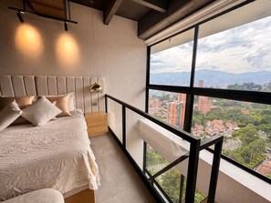 A bedroom with a large window, a bed, and a nightstand. - Luxury Duplex with City Views (Medellín)