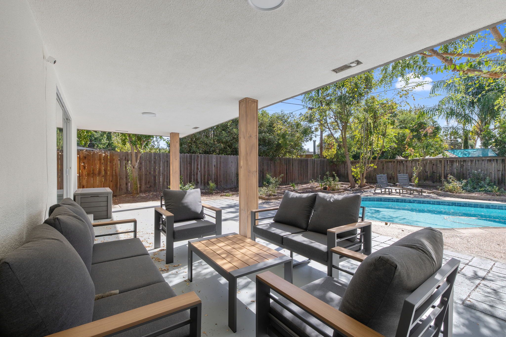 An outdoor patio with a pool, grey furniture, and a wooden fence in the background.
