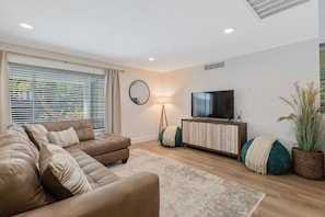 A modern living room with a sofa, TV, lamp, and decorative plants.