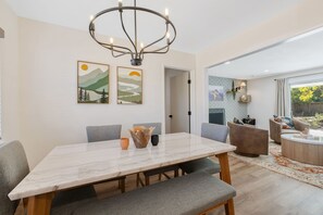 A modern dining area with a marble table, grey upholstered chairs, and a chandelier.
