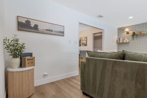 Una sala de estar moderna con un sofá verde, una mesita de madera con un letrero de bienvenida y un cuadro de paisaje enmarcado en la pared.