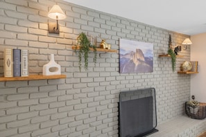 A living room with a white brick fireplace, bookshelves with decorative items, and wall-mounted lamps.