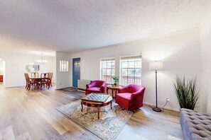 Step into your bright, open living space where natural light pours through large windows, inviting you to relax in the cozy sitting area or gather around the dining table just beyond. - Creekside Sugar Mountain Cabin with Fireplace (Sugar Mountain)