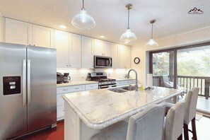 A modern kitchen with stainless steel appliances, a central island with seating, and a view to a deck. - Elegant 2 Bedroom Condo on the Golf Course at Sugar Mountain (Sugar Mountain)