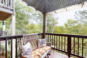 Una terraza de madera con un banco y una mesita, rodeada de abundante vegetación.