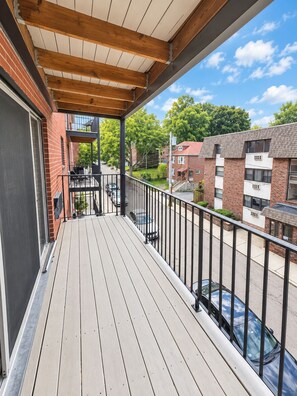 Eine Holzterrasse mit Metallgeländer, die auf eine Straße mit Autos und Gebäuden blickt.