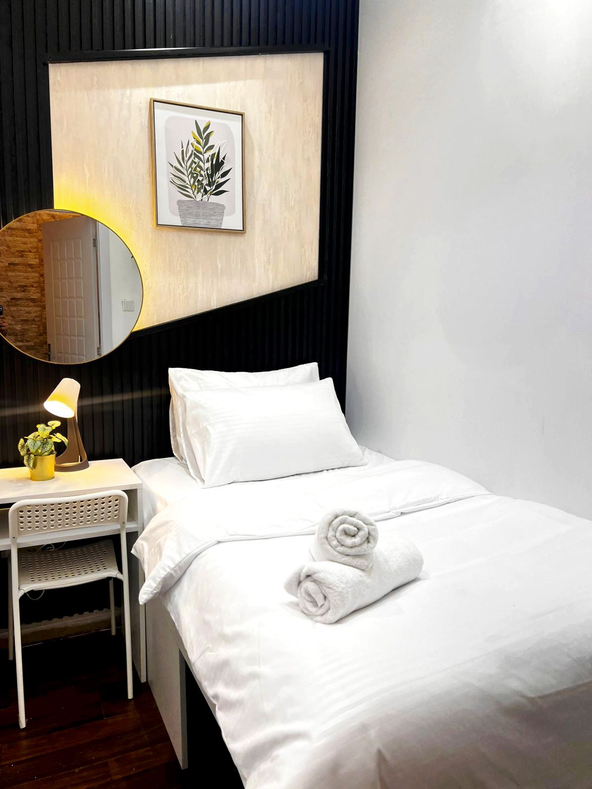 Een hotelkamer met een bed, een nachtkastje met een lamp, een spiegel en een ingelijst schilderij aan de muur.