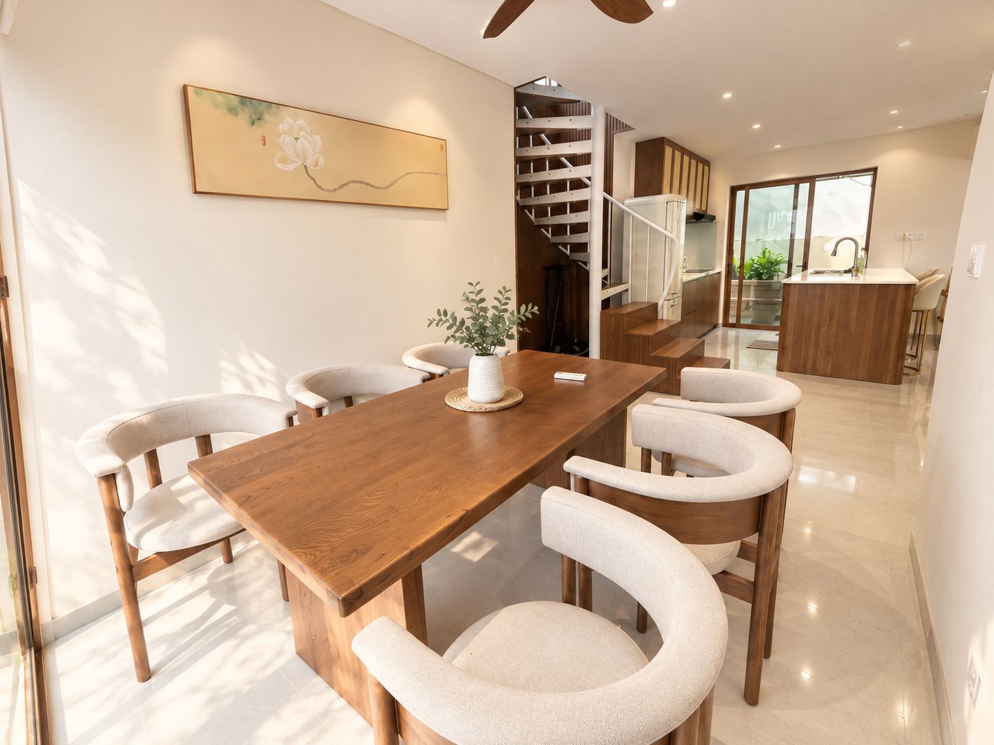 A modern dining area with a wooden table and chairs, a staircase, and a kitchen area.