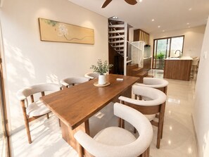 A modern dining area with a wooden table and chairs, a staircase, and a kitchen area. - Beachfront Villa Gành Dầu 5Brs by Anamoi (Phú Quốc)