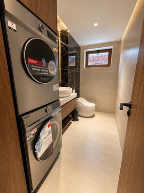 Une salle de bain moderne équipée d’un lave-linge et d’un sèche-linge intégrés, de toilettes et d’un meuble-lavabo avec un miroir.
