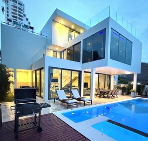 Ein modernes, zweistöckiges Haus mit Schwimmbad, Außenbereich mit Sitzgelegenheit und einer sichtbaren Treppe.