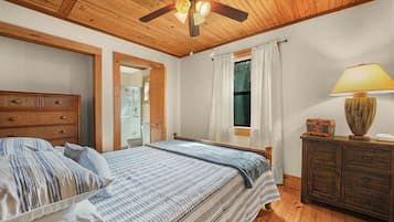 A bedroom with a wooden ceiling, a bed with striped bedding, a nightstand with a lamp, and a window with curtains.
