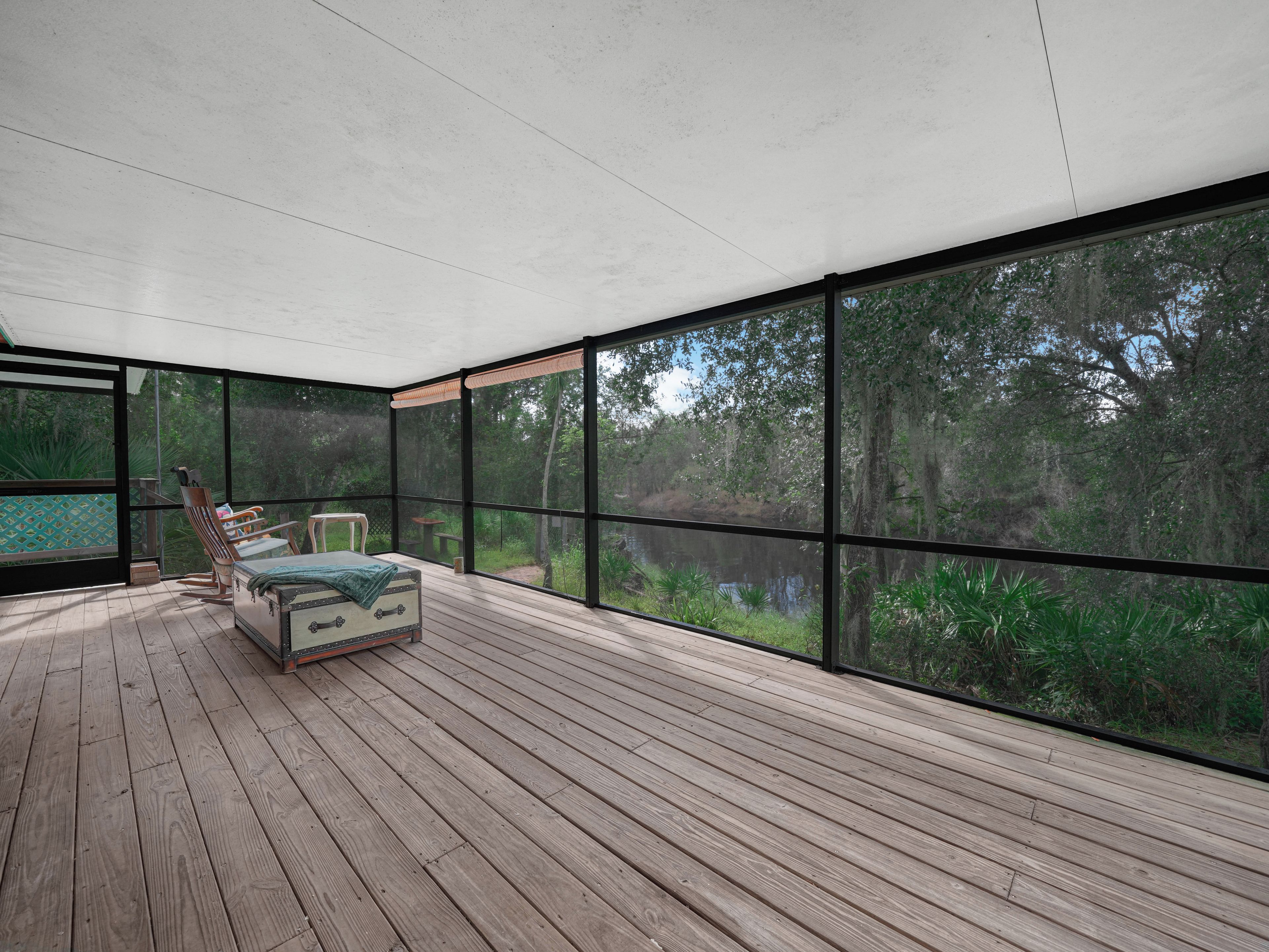 Una habitación amplia con una cama grande, piso de madera y vistas a un bosque a través de amplios ventanales.