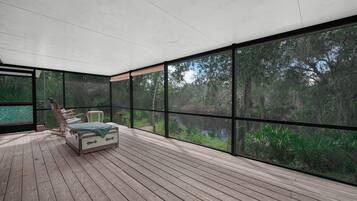 Una habitación amplia con una cama grande, piso de madera y vistas a un bosque a través de amplios ventanales.