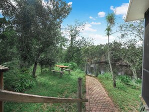 A pathway leading to a picnic table and a small pond, surrounded by lush greenery and trees. - Enjoyable 1-bedroom cabin with AC in charming Arcadia on Peace River (Arcadia)