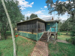 A house with a screened porch, a wooden deck, and a brick pathway leading to the entrance. - Enjoyable 1-bedroom cabin with AC in charming Arcadia on Peace River (Arcadia)