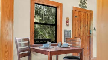A wooden dining table with four chairs, a window with a view of trees, and a wooden door with a plaque.