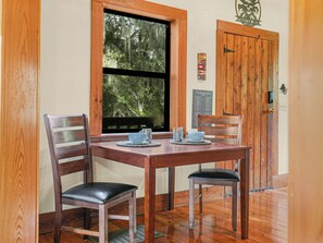 A wooden dining table with four chairs, a window with a view of trees, and a wooden door with a plaque.