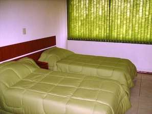 A room with two beds, a wooden headboard, a window with blinds, and a tiled floor. - Hotel Ouro Verde (Charqueadas)