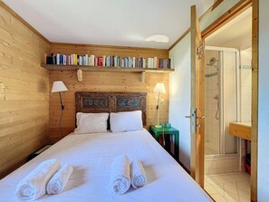 Ein Zimmer mit Holzwänden, einem Bett, zwei Nachttischlampen, einem Bücherregal und einem Duschbereich.