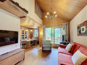 Ein gemütliches Wohnzimmer mit Fernseher, Holzmöbeln, einem roten Sofa und einem Essbereich mit Tisch und Stühlen.