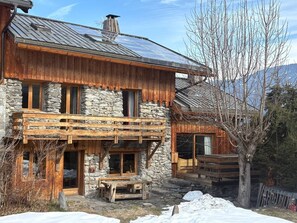 A rustic cabin with a stone facade, wooden balconies, and a clear view of the surrounding mountains.