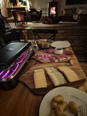 Ein Holztisch mit einer Wurst- und Käseplatte, einem Grill und einem Kamin im Hintergrund.