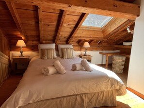 Ein Schlafzimmer mit einem großen Bett, Holzbalkendecke, Dachfenster und Nachttischlampen.