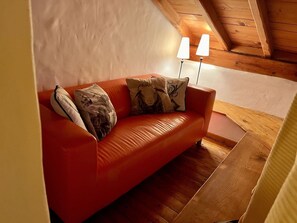 En rød lædersofa med mønstrede puder i et rum med trægulv og skrå væg.