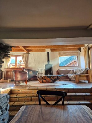 A cozy living room with a fireplace, wooden furniture, and a stone wall.