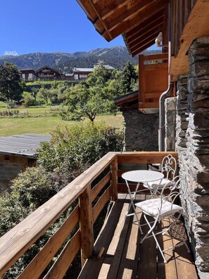 Eine Holzterrasse mit einer Steinmauer und einem Tisch mit Stühlen, mit Blick auf eine gebirgige Landschaft.