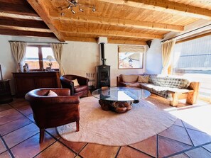 Un salon chaleureux avec un plafond en bois, une table basse ronde en verre, des fauteuils en cuir, un canapé et un poêle à bois.