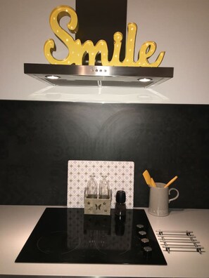 Eine Küche mit einer Edelstahl-Dunstabzugshaube, einer schwarzen Induktionskochplatte und einer Spritzschutzwand mit geometrischem Muster.