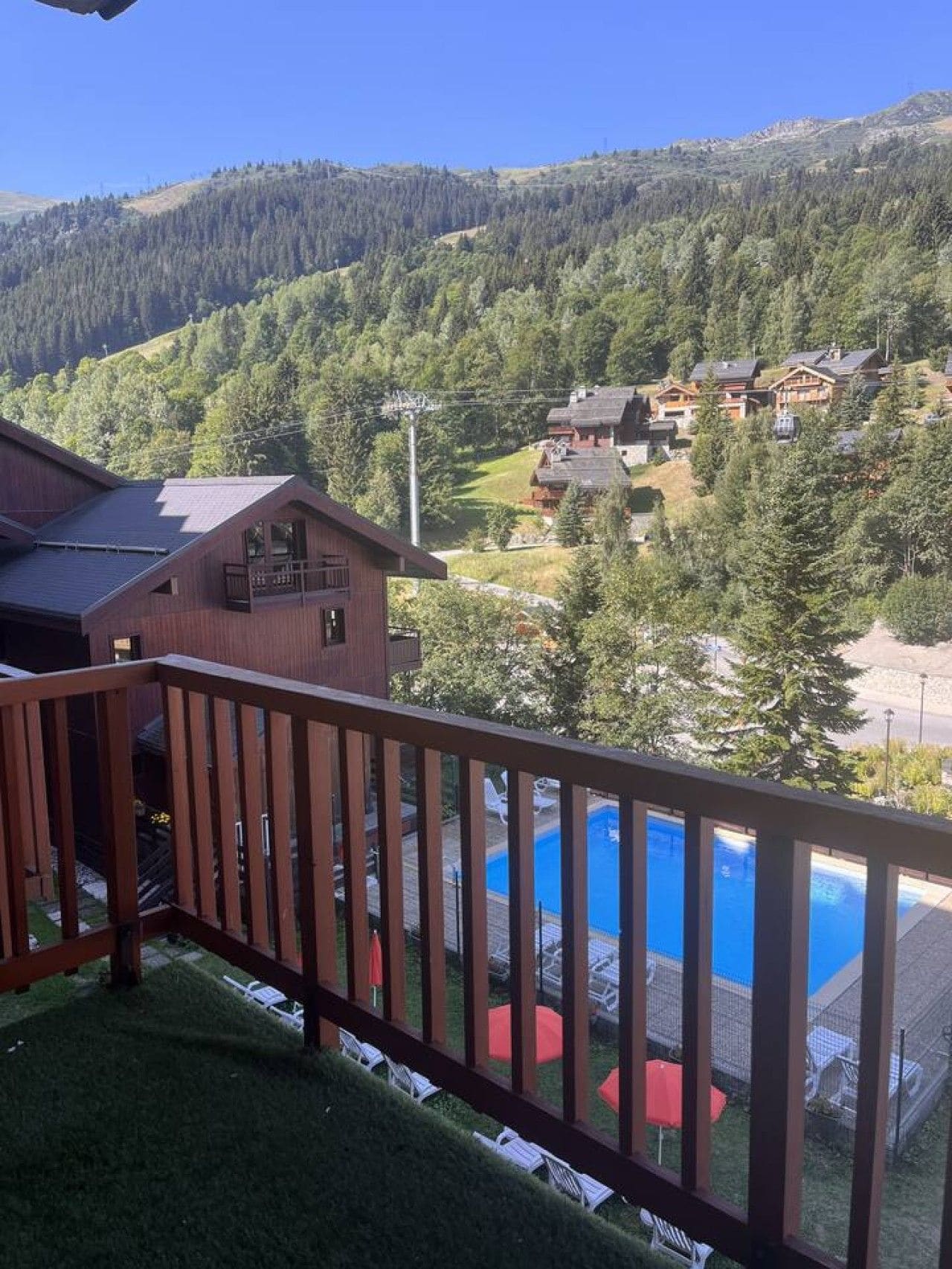A wooden balcony with a view of a swimming pool and surrounding buildings.