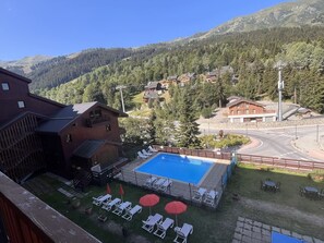 Área de piscina com espreguiçadeiras e guarda-sóis, emoldurada por uma paisagem montanhosa.