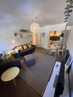 Een moderne woonkamer met een bank, een pouf en een eethoek met stoelen en een tafel.