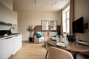 A modern kitchen with a dining area, a sofa, and a TV mounted on the wall. - Apartament z Balkonem Kamienica przy R. Łazarskim (Poznań)
