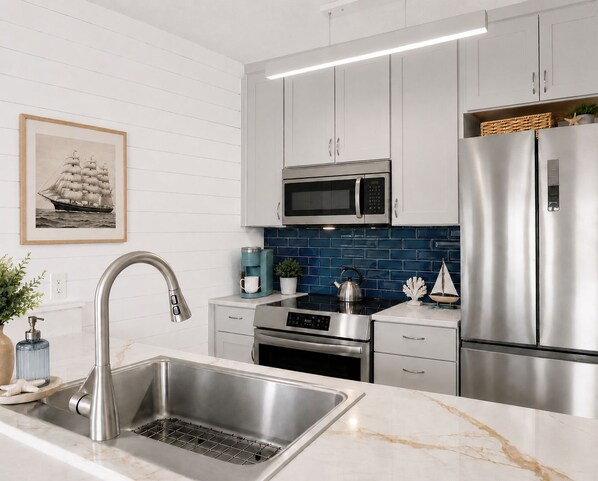 A modern kitchen with stainless steel appliances, a white backsplash, and a framed picture on the wall. - Nigh Noon - Ocean view, 50 yards to the beach (Surf City)