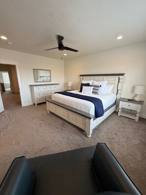 Une chambre à coucher comprenant un lit, une commode, une table de chevet, un ventilateur de plafond et une chaise.