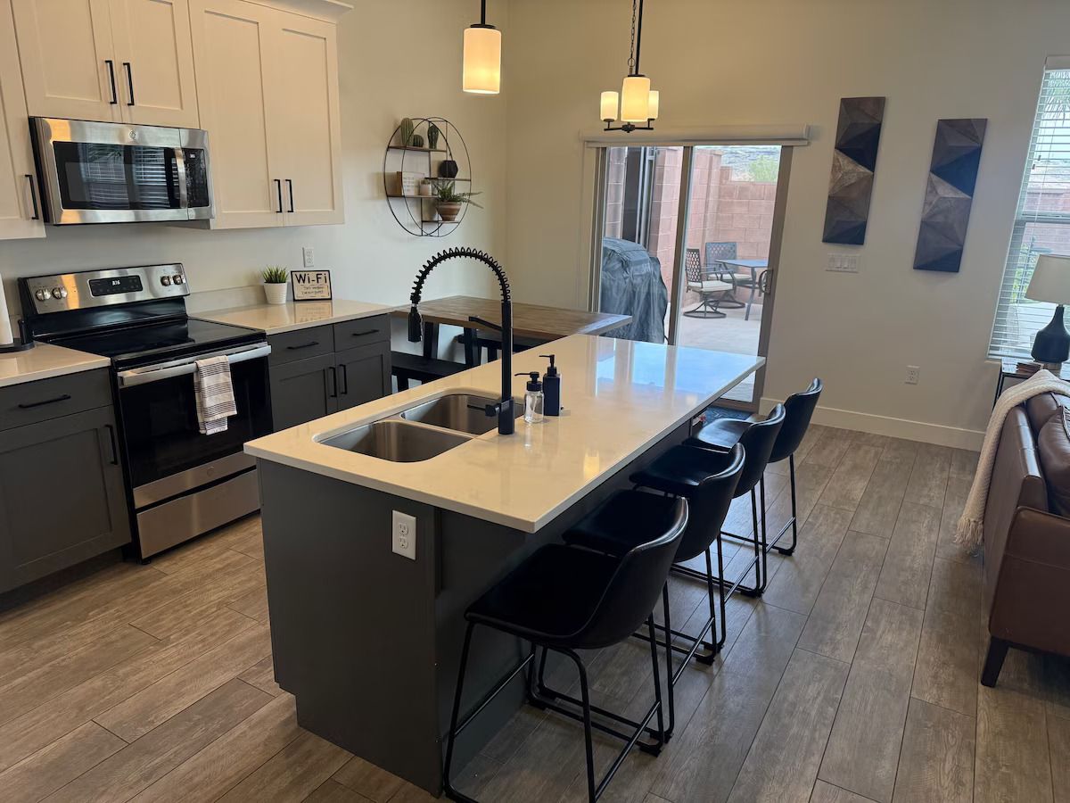 A modern kitchen with a central island, bar stools, and a dining area with a view to the outdoors.