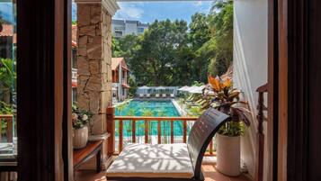 A balcony with a view of a swimming pool, a stone wall, and a chair.