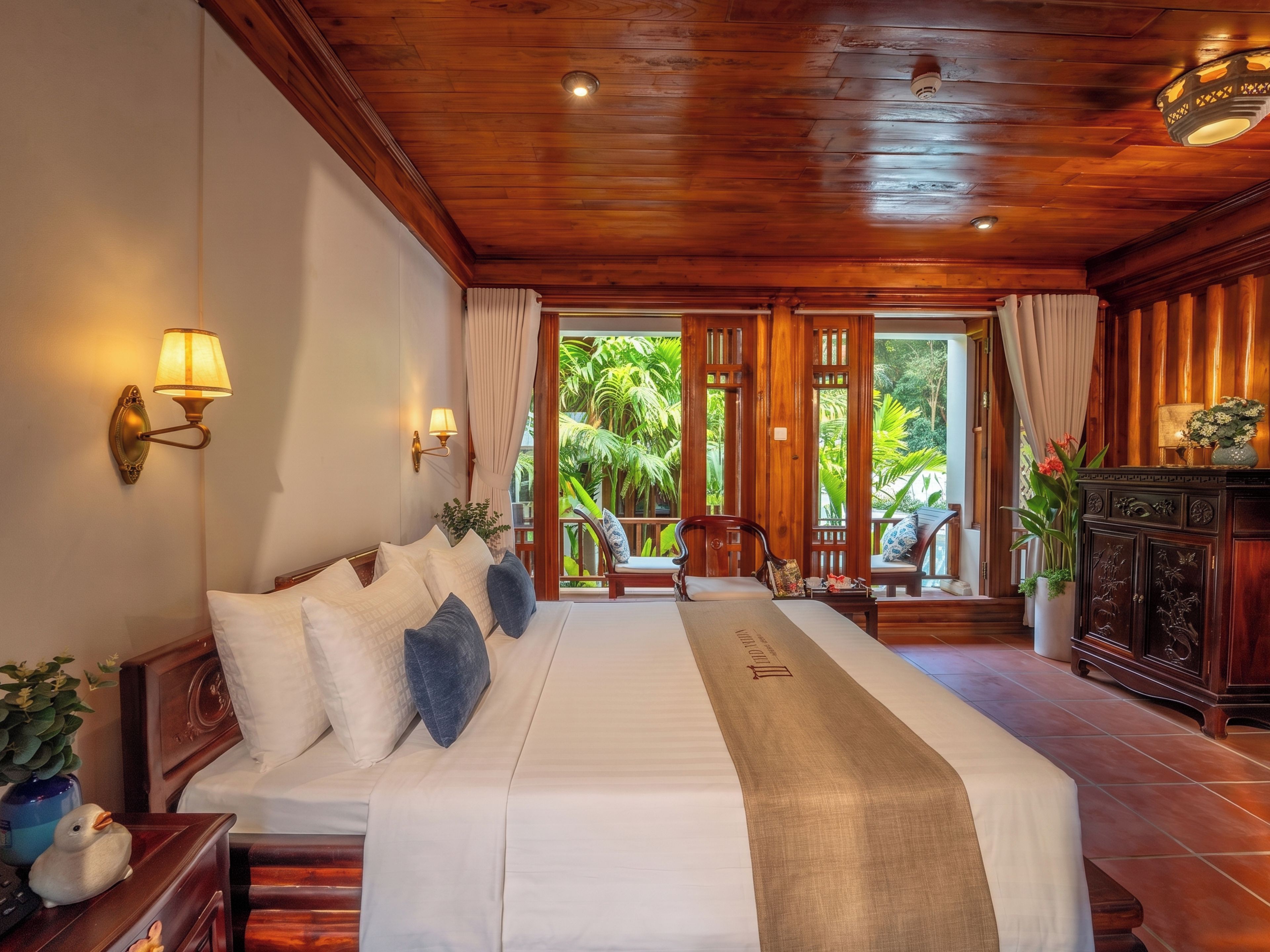 Habitación de hotel con una cama grande, techo de madera y vistas a vegetación exuberante.